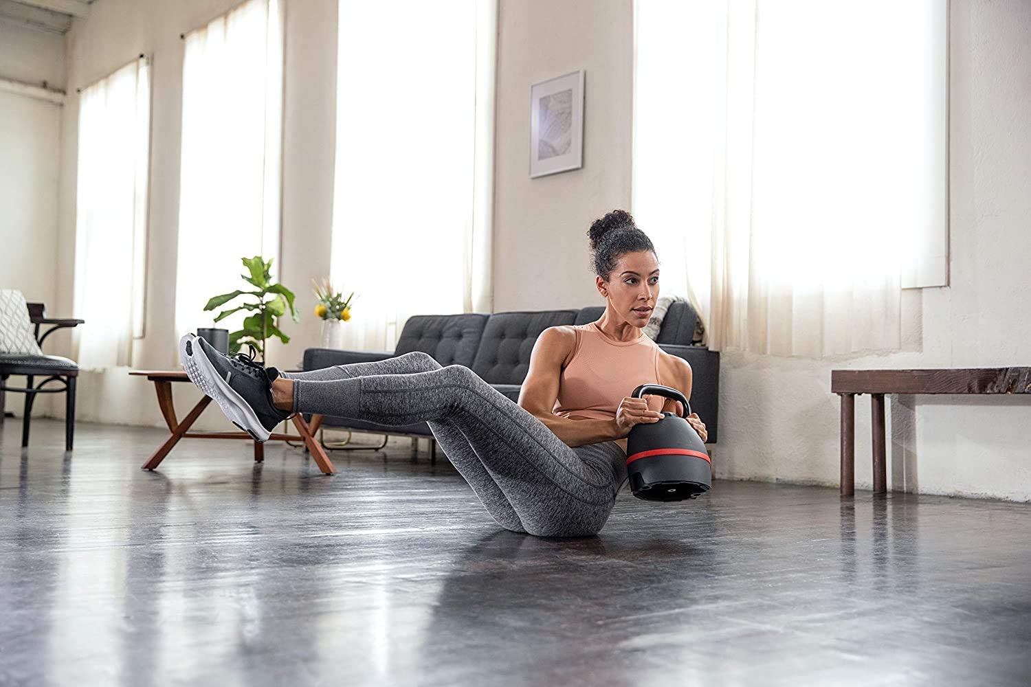 Woman using the Bowflex SelectTech Kettlebell in a twist weight pilated exercise while seated on the floor of her living room.