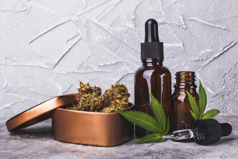 Cannabis oil extracts in droppers beside marijuana leaves and marijuana cones in a metal container