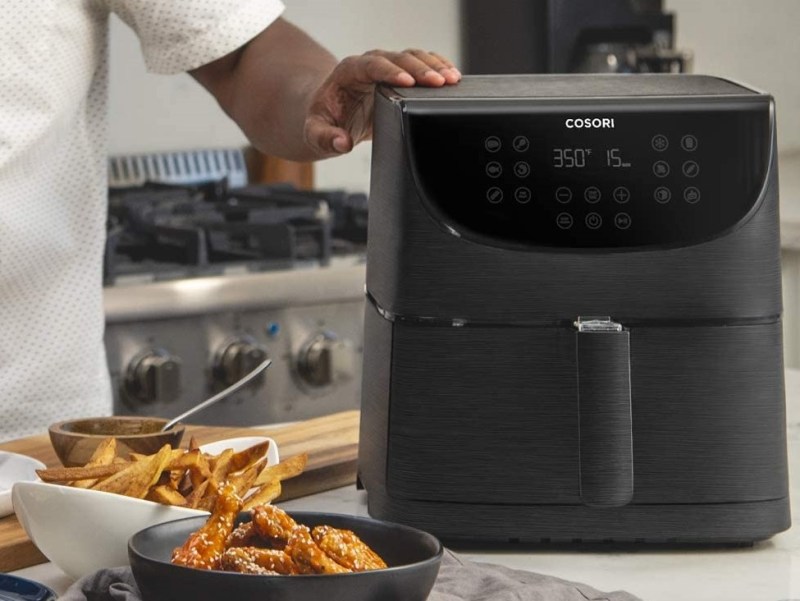 COSORI Air Fryer Max XL on counter with chef cooking.