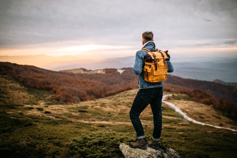 A man carrying an orange backpack enjoying the view from a mountain top.