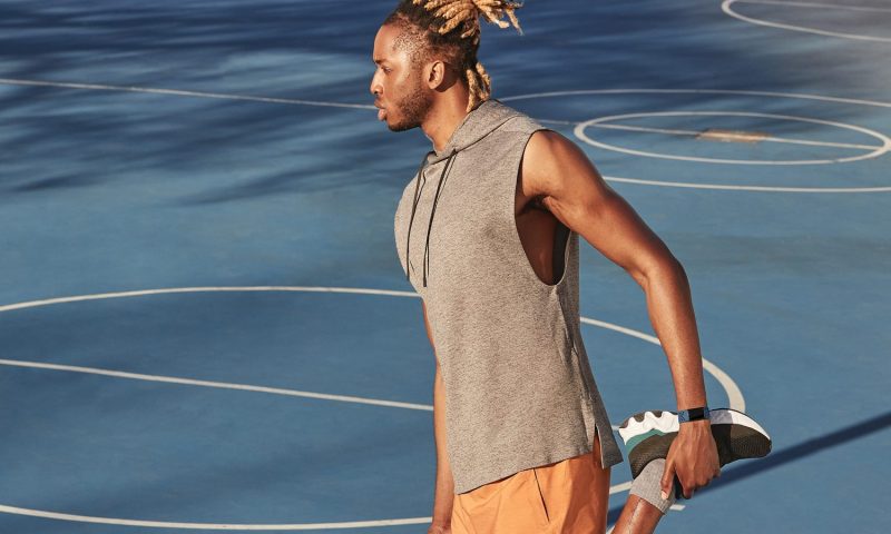 A male athlete with Fitbit tracker stretching at a basketball court.