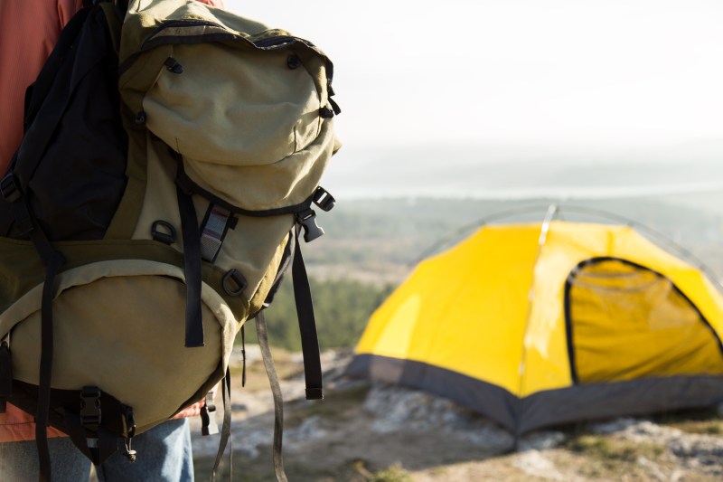 Big camping green backpack and yellow tent in the mountains.
