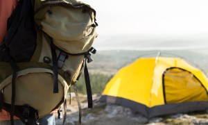 Big camping green backpack and yellow tent in the mountains.