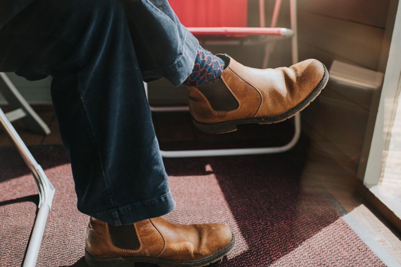 Male wearing Brown Leather Chelsea Boots, legs crossed at the knee, sitting in a sun room.