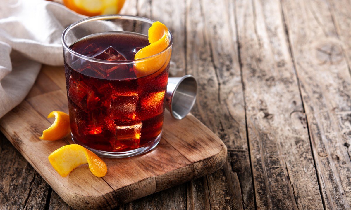 A Boulevardier cocktail with orange skin on a wooden table.