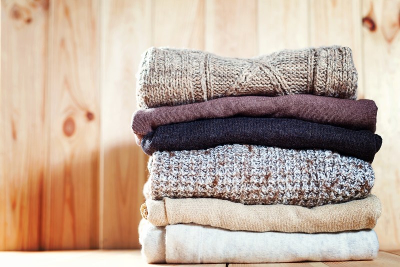 Knit cozy sweater folded in piles on a wooden background.