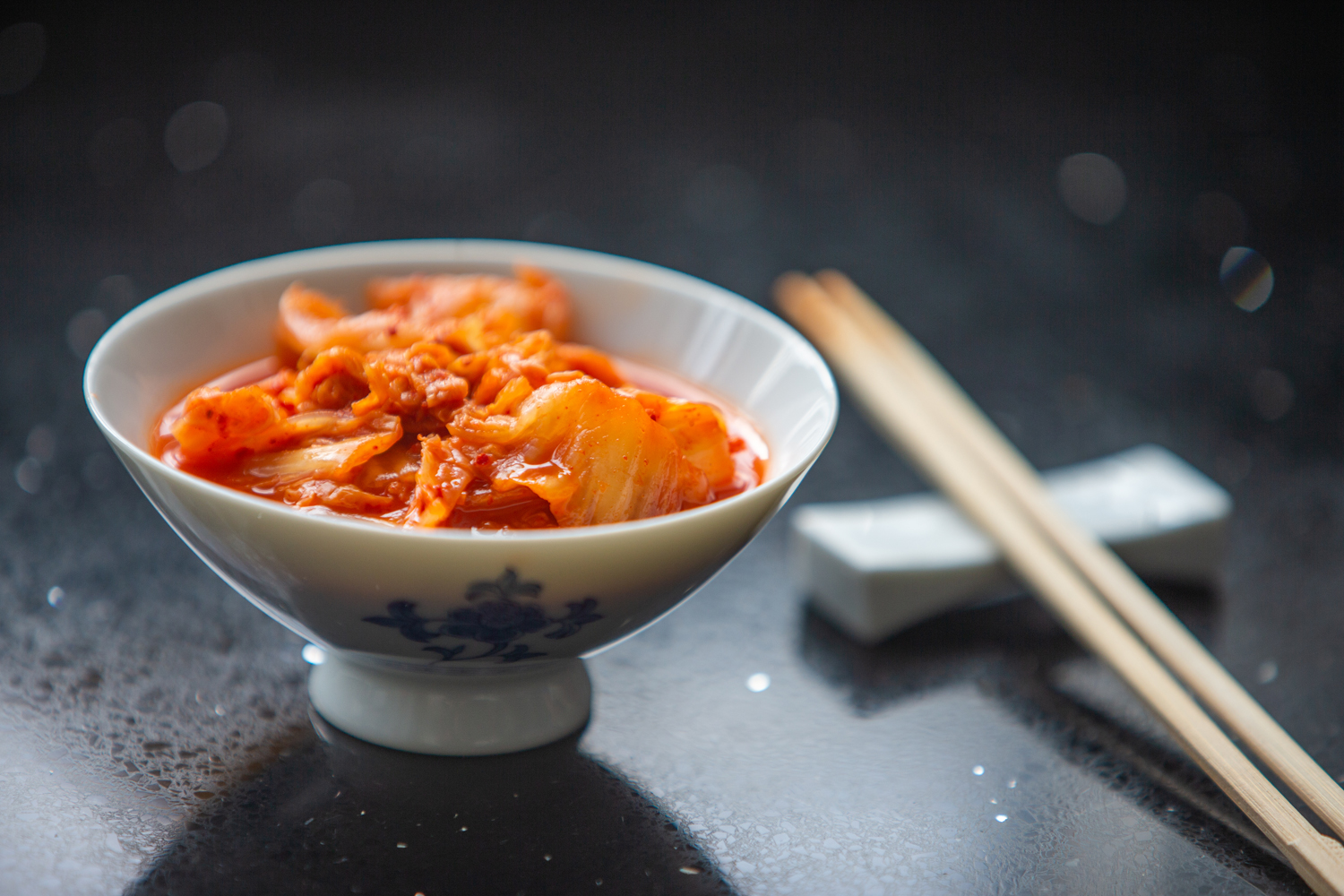Kimchi served in a porcelain bowl beside chopsticks.
