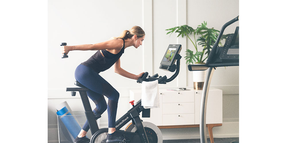 A woman riding a NordicTrack Commercial S15i Studio Cycle while holding a dumbbell.