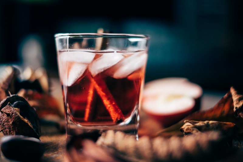 An apple cider cocktail with ice and cinnamon sticks.