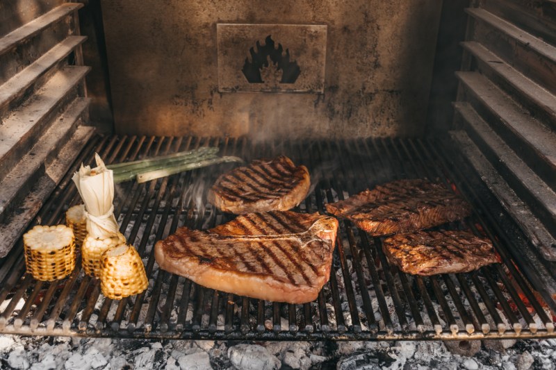 steaks and corn being grilled over a charcoal grill.