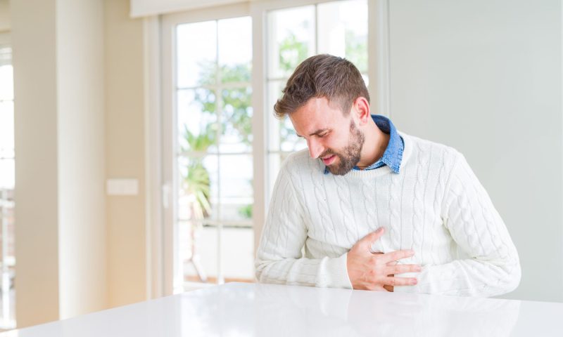 A man in white sweater touching his aching stomach.