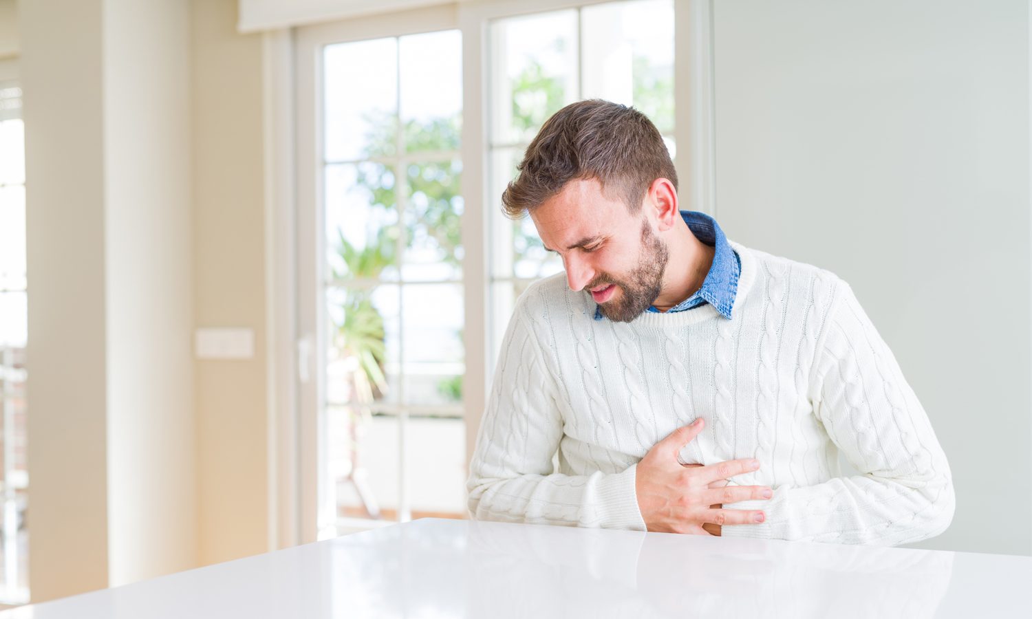 A man in white sweater touching his aching stomach.