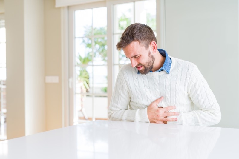 A man in white sweater touching his aching stomach.