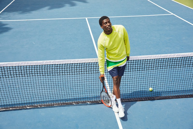 Lifestyle image of man standing on tennis court wearing Wilson sportswear.