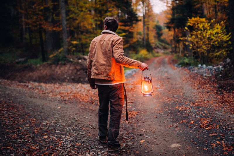 A man with a lantern at a crossroads in the woods.