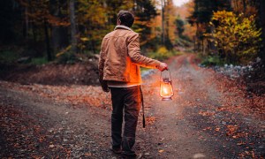 A man with a lantern at a crossroads in the woods.
