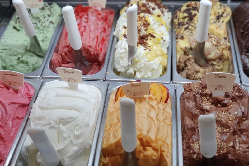 pans of different flavored ice cream with scoops in each one.