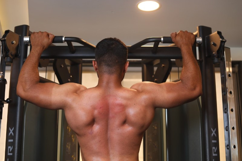 Shirtless man doing a shoulder workout on a pull-up bar.