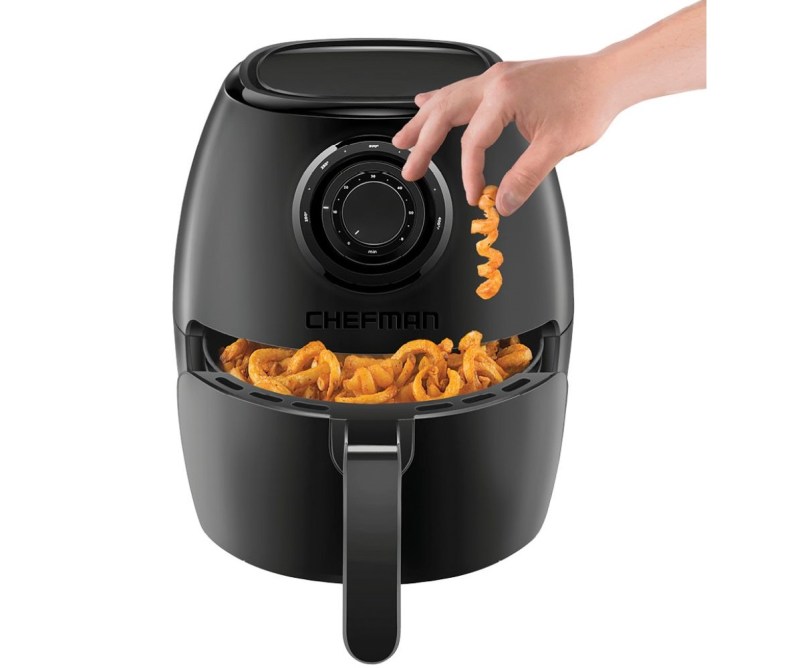 Chefman Turbofry Air Fryer full of curly fries with a hand picking one up, on a white background.