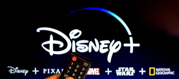 Close-up of a hand holding a remote navigating to Disney Plus on a TV .