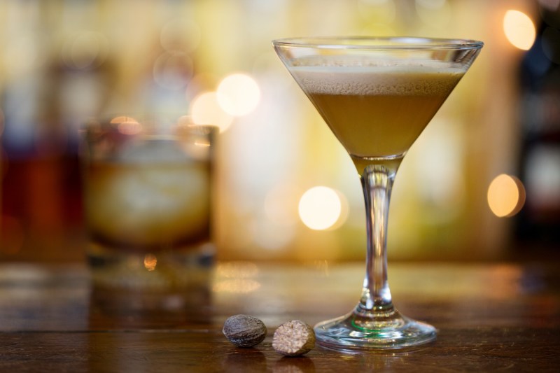 Een glas Brandy Alexander met een kopje cocktail erachter op een tafel.