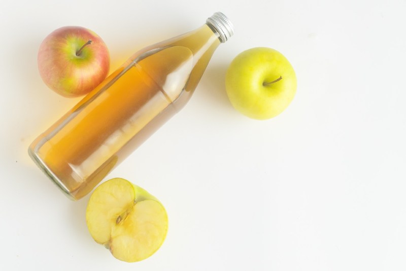 three apples and one bottle of hard cider on a table.