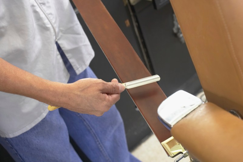 A midsection of a barber sharpening a straight razor.