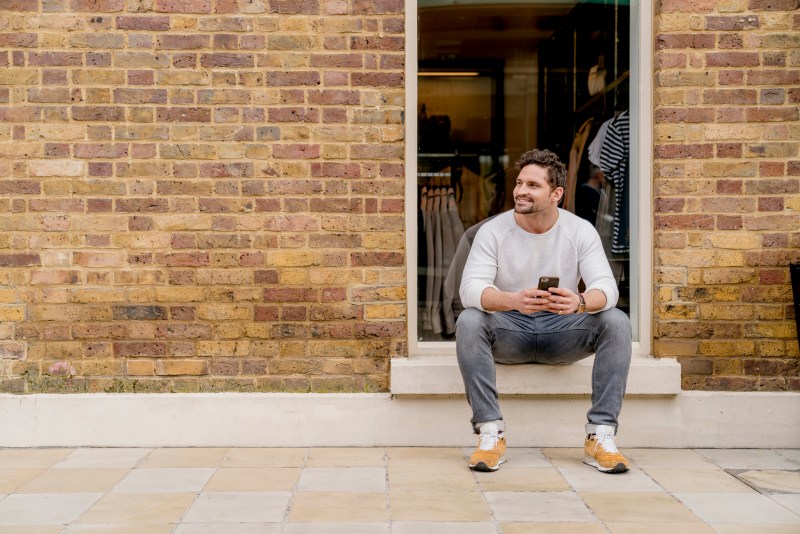 Young man with smartphone sitting on doorstep, Kings Road, London, UK.