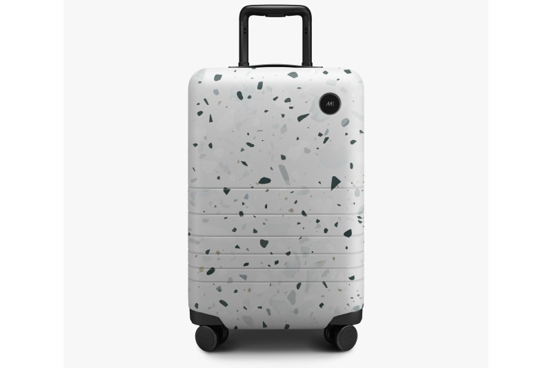 monos carry on luggage against a gray background.