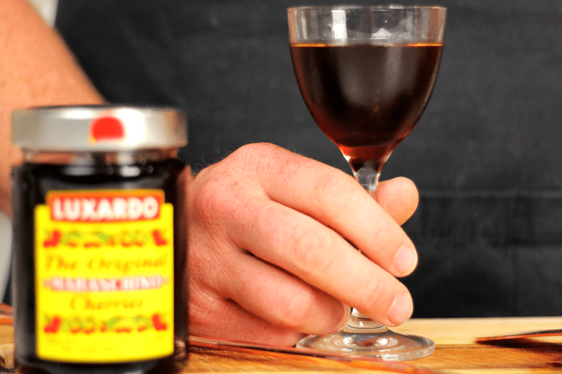 Een close-up van de hand van Steve de barman die een glas Reverse Manhattan vasthoudt.