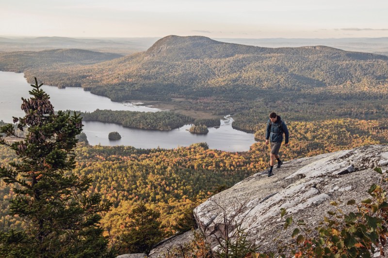 male hiker walks along cliff with view on Appalachian Trail, Maine.