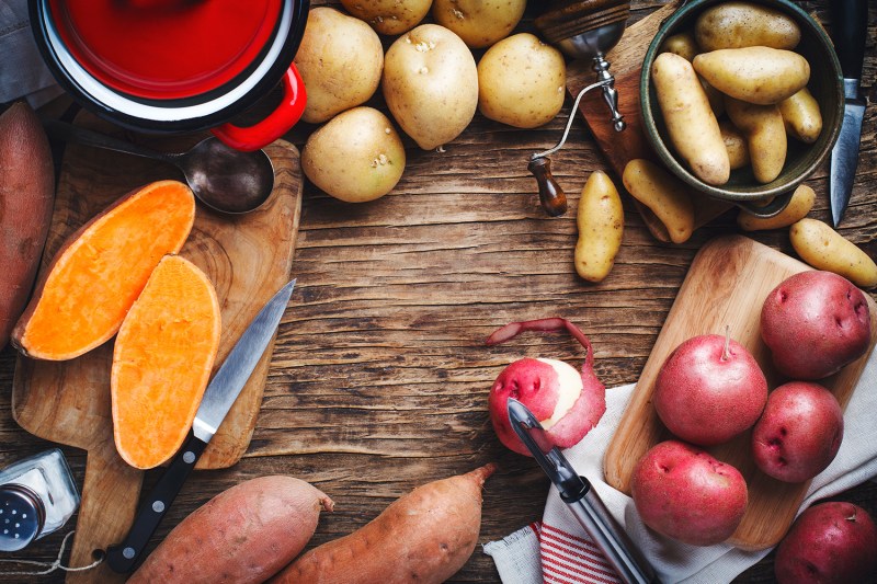 Variety of raw uncooked organic potatoes: red, white, sweet and fingers potatoes over wooden background.