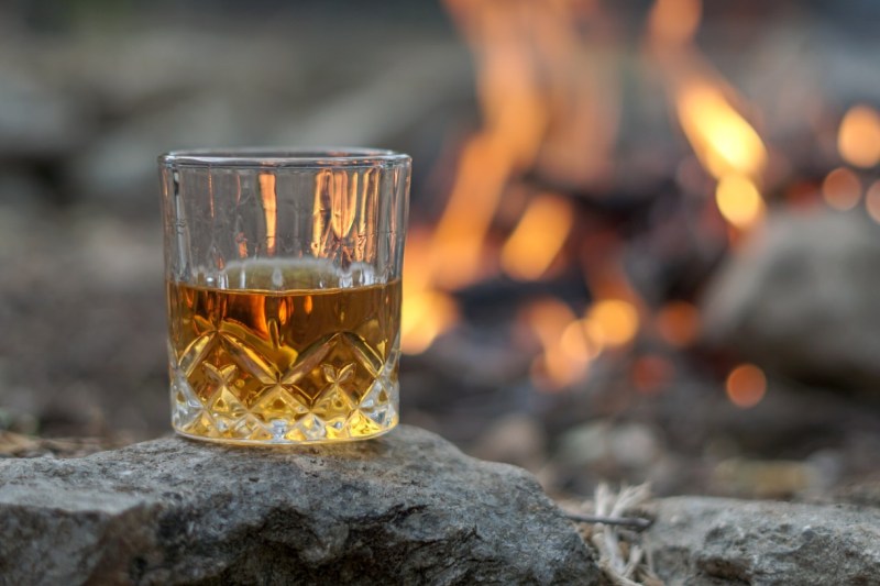 Whiskey in a crystal glass sitting on a rock in front of a fire.