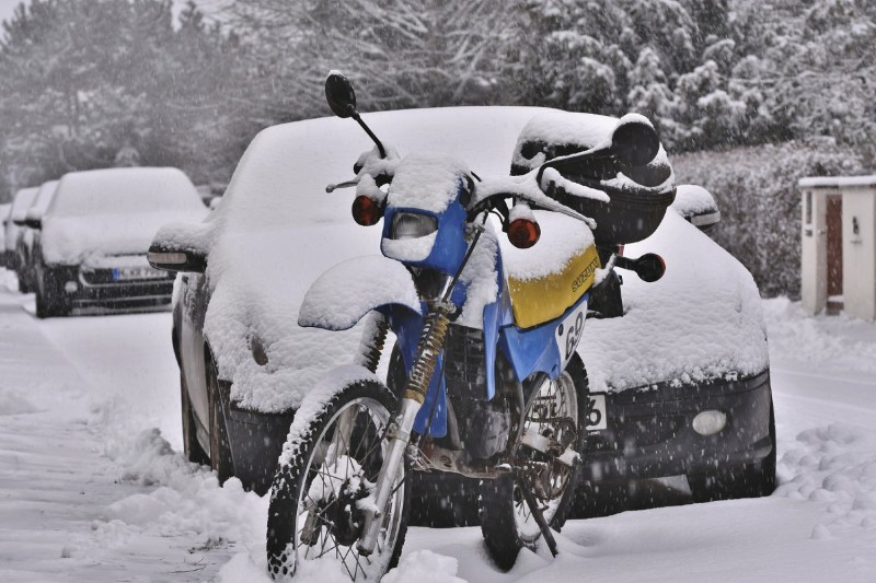 motorcycle standing in front of a car covered in snow.