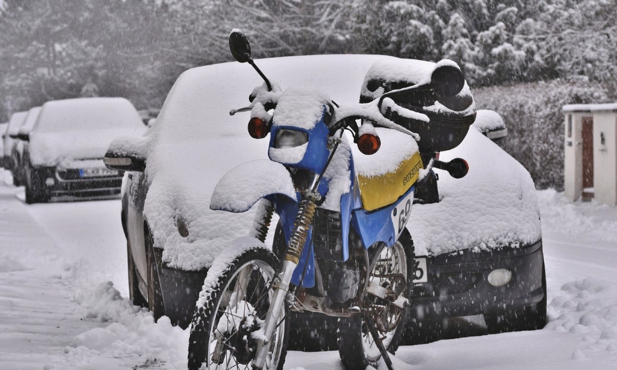 motorcycle standing in front of a car covered in snow.