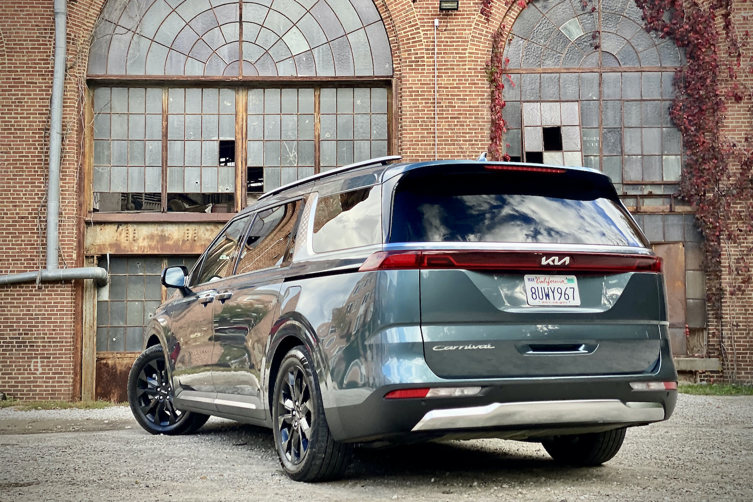 Kia Carnival rear end from driver side with old building in the background.