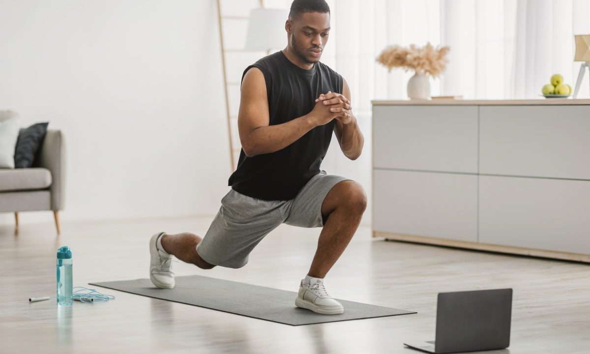 Man doing alternating forward lunges in front of a laptop at home.