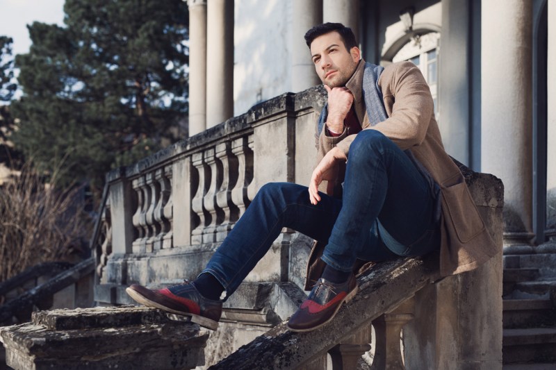 A man in jeans posing on a railing of an old mansion.