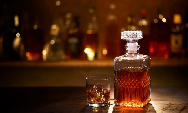 A bourbon whiskey decanter and bourbon on the rocks in a tumbler sitting on a bar with bottles in the background