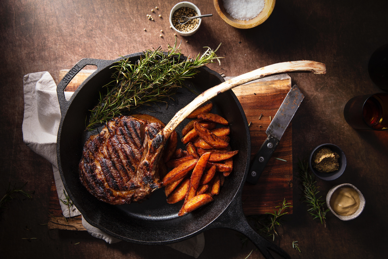 Bone-in, cowboy cut ribeye in a cast iron with fries.