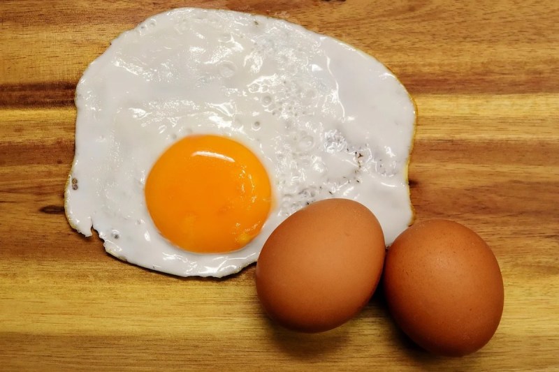 two brown eggs sitting next to a sunnyside up egg on a cutting board.