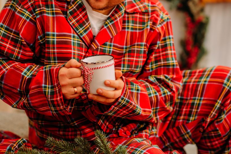 A midsection of a man wearing checkered pajamas and holding a mug at home.