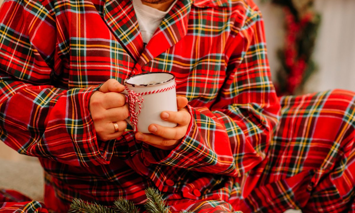 A midsection of a man wearing checkered pajamas and holding a mug at home.