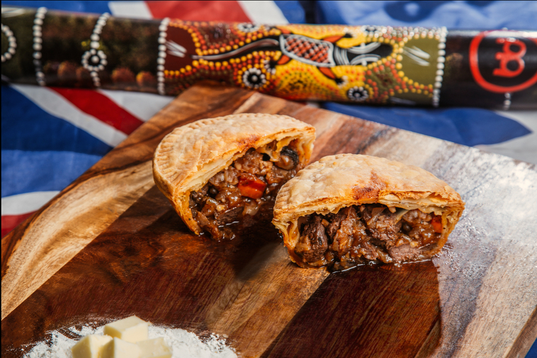 G'day Gourmet meat pie cut in half on cutting board with Australian flag in background.