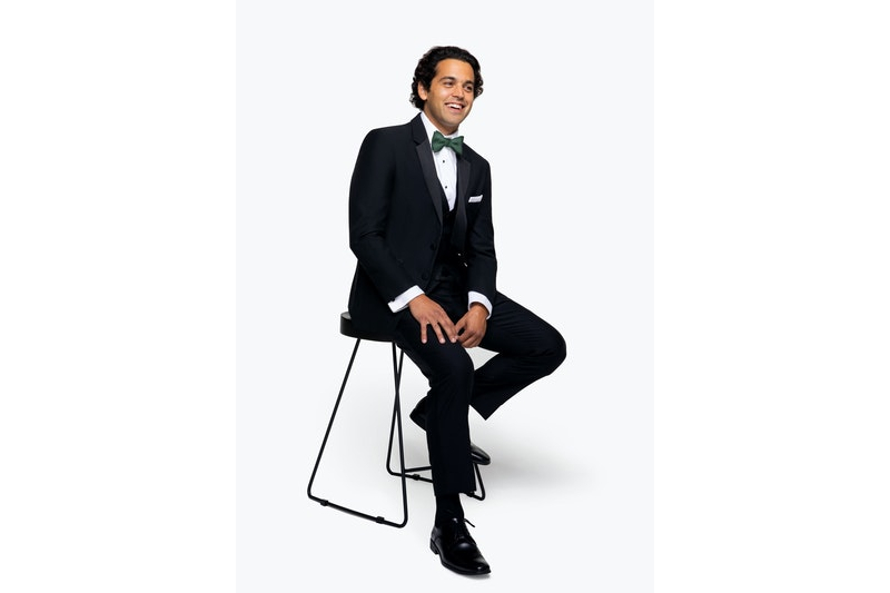 man in a tuxedo sitting on a stool.