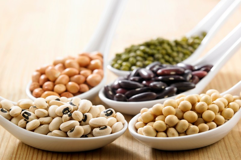 A variety of legumes on white spoons.