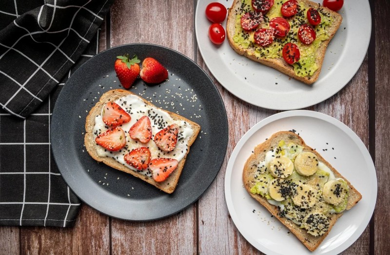 three whole grain pieces of toast on plates with fruits and vegetables.