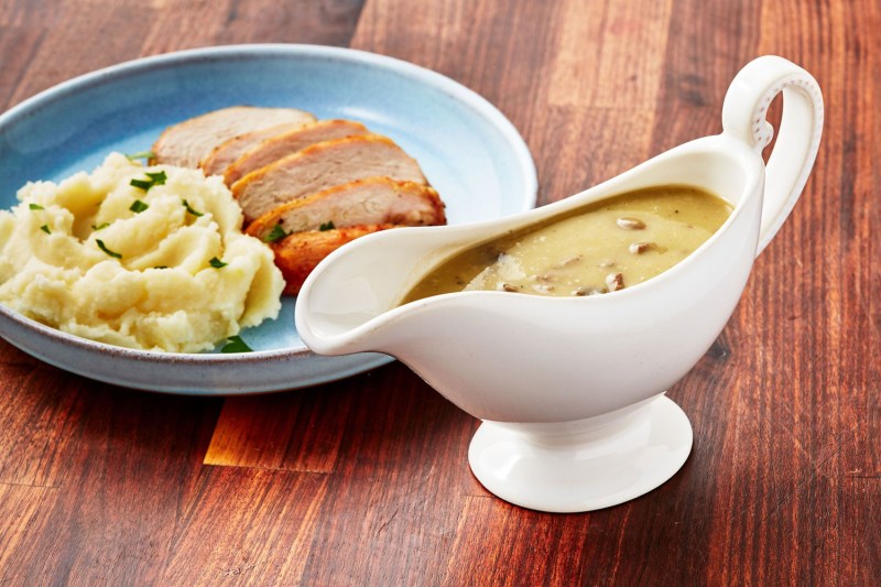 A giblet gravy served in a gravy boat beside a plate of turkey-based dish.