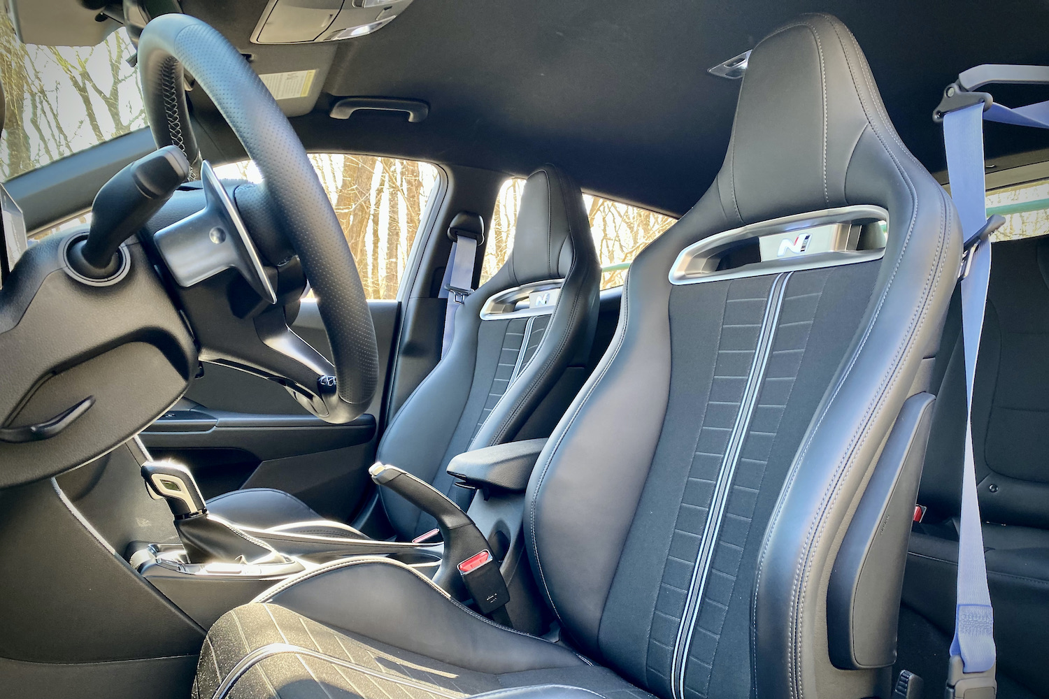 Hyundai Veloster N close up of front drivers seat with blue seat belt and trees in the background.