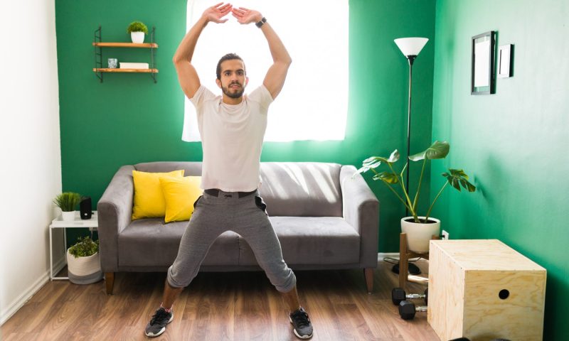 A man doing jumping jacks in his bedroom.